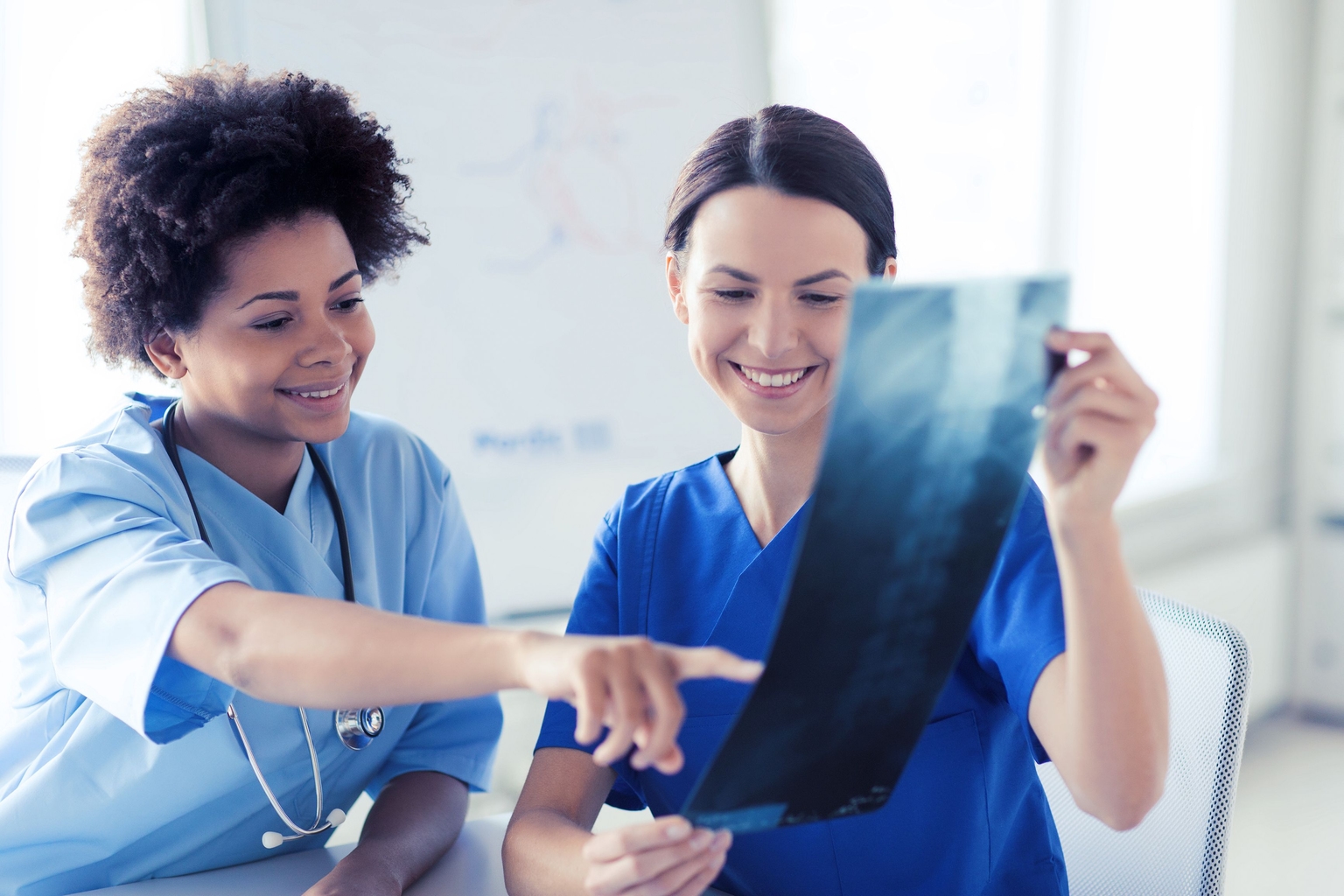 Two radiography techs reviewing an X-ray image together, with one tech pointing at a specific area on the X-ray and the other smiling.